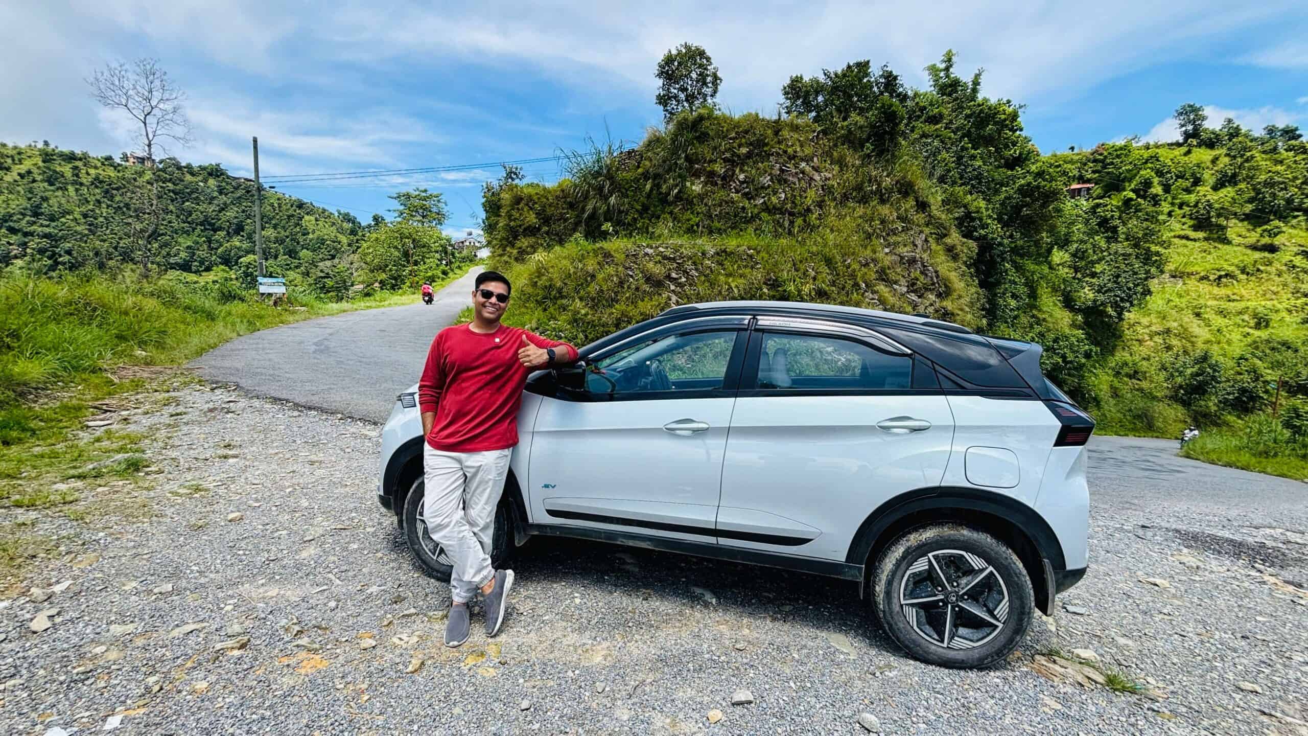 Modern electric SUV parked on scenic mountain road with lush greenery and blue sky; outdoor adventure, eco-friendly vehicle, and travel photography.